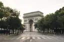 An empty tree-lined avenue leading to the Arc de Triomphe in soft early light