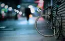 A bicycle on a city pavement at night, street lights glowing behind