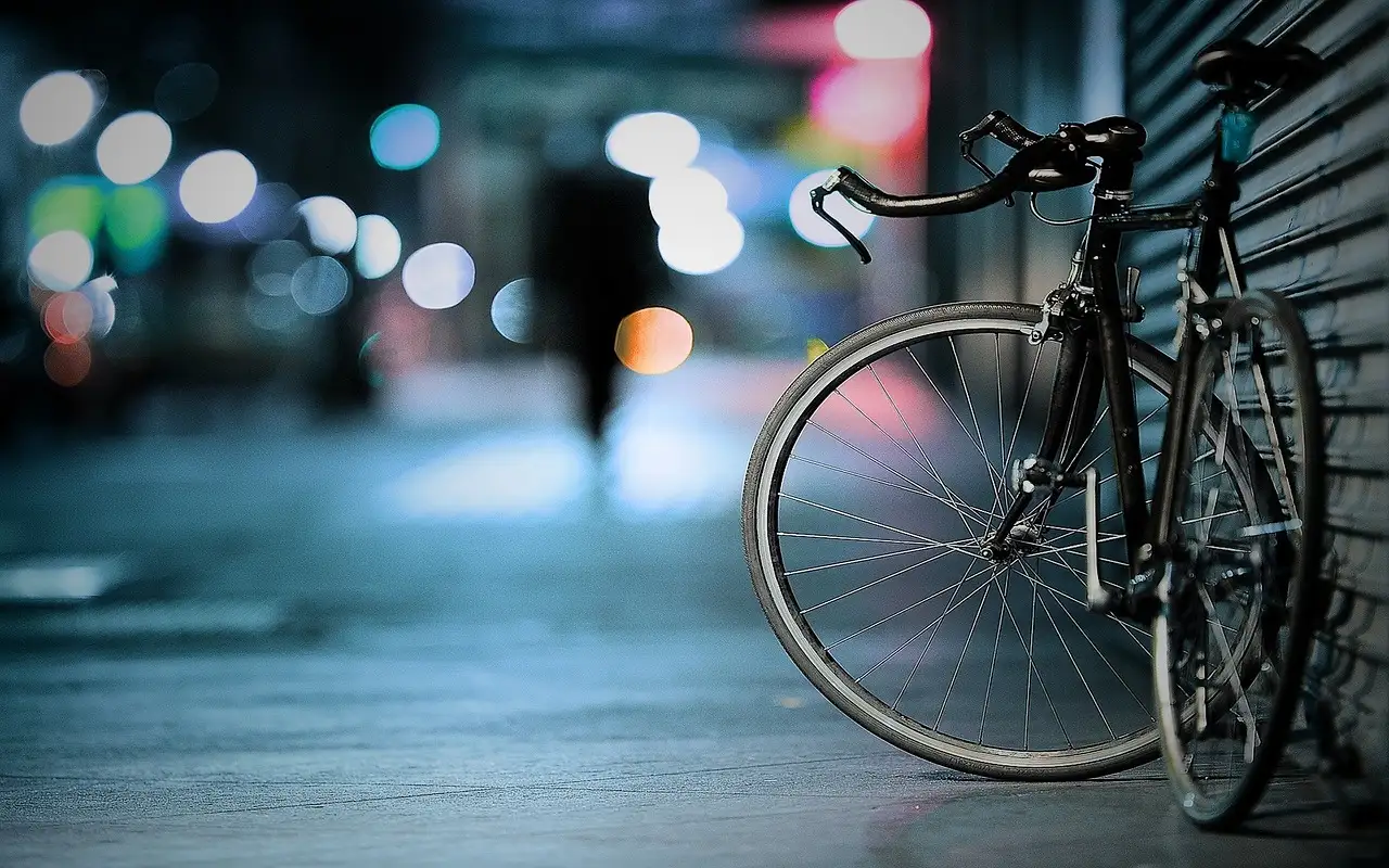 A bicycle on a city pavement at night, street lights glowing behind