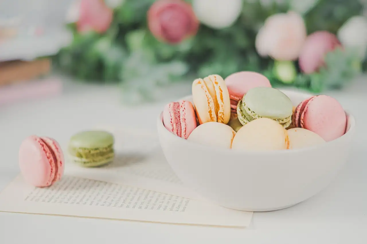A white bowl of pastel macarons on a light table