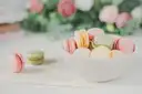 A white bowl of pastel macarons on a light table
