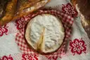 A whole Camembert cheese on a red checked cloth with bread