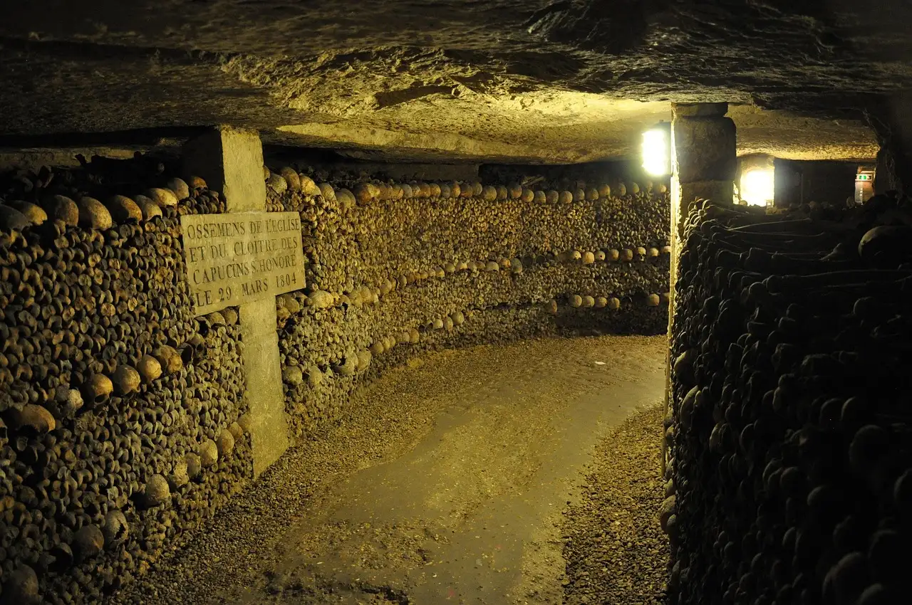 A lit gallery in the Paris Catacombs lined with walls of stacked bones and skulls