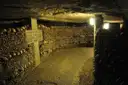 A lit gallery in the Paris Catacombs lined with walls of stacked bones and skulls