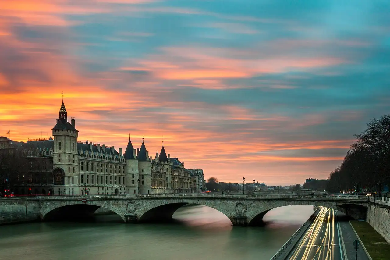 The Conciergerie and a Seine bridge under a bright sunset sky