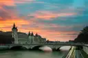 The Conciergerie and a Seine bridge under a bright sunset sky