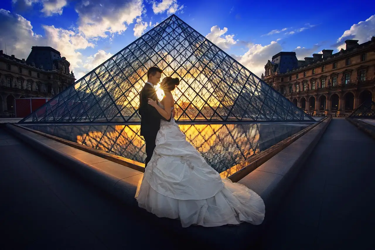 A couple posing in front of the Louvre pyramid at sunset
