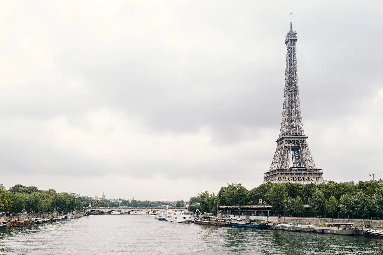 The Eiffel Tower rising above the trees along the Seine on a cloudy day