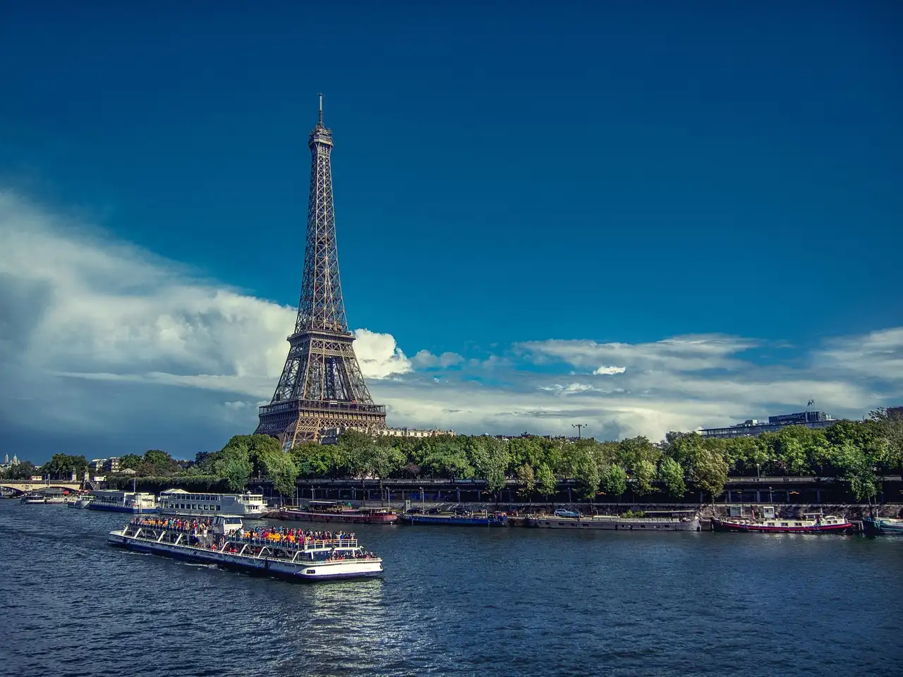 A sightseeing boat on the Seine below the Eiffel Tower under a deep blue sky