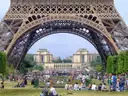 The base of the Eiffel Tower framing the Trocadéro, people sitting on the lawn