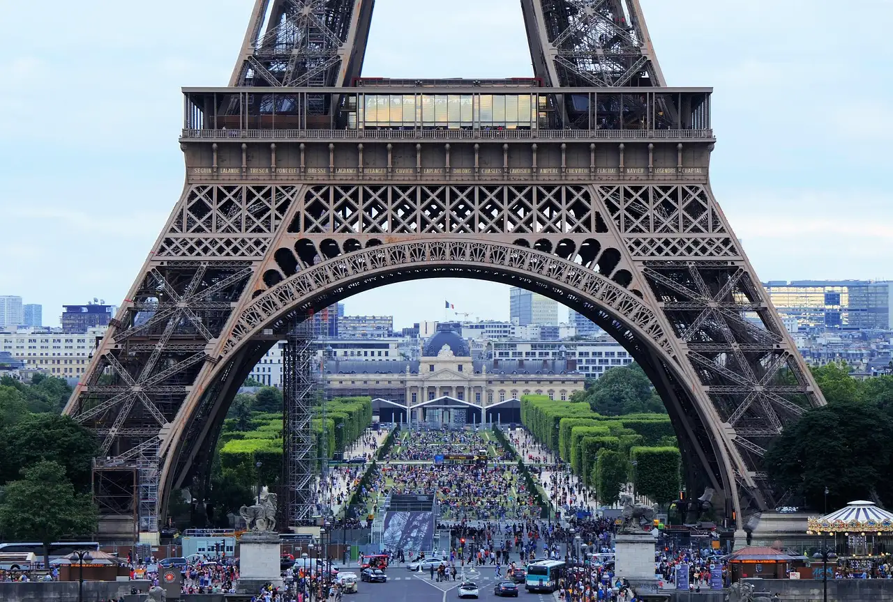 The Eiffel Tower's first-level arch framing the Champ de Mars and the crowds beneath it