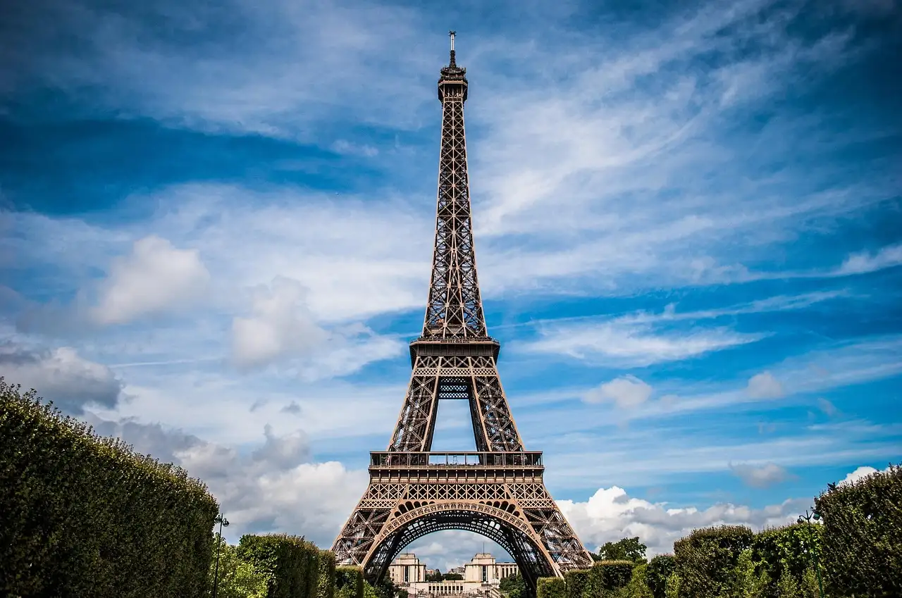 The Eiffel Tower under a blue sky with streaks of cloud, seen from the gardens below