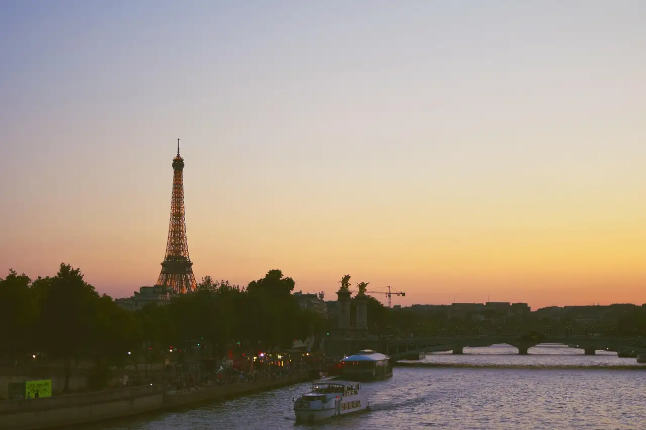 The Eiffel Tower above the Seine at sunset, with a boat on the river