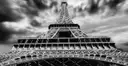 Black-and-white view up through the Eiffel Tower's iron lattice under a cloudy sky