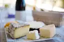 A board of French cheeses on a table with a bottle of wine behind