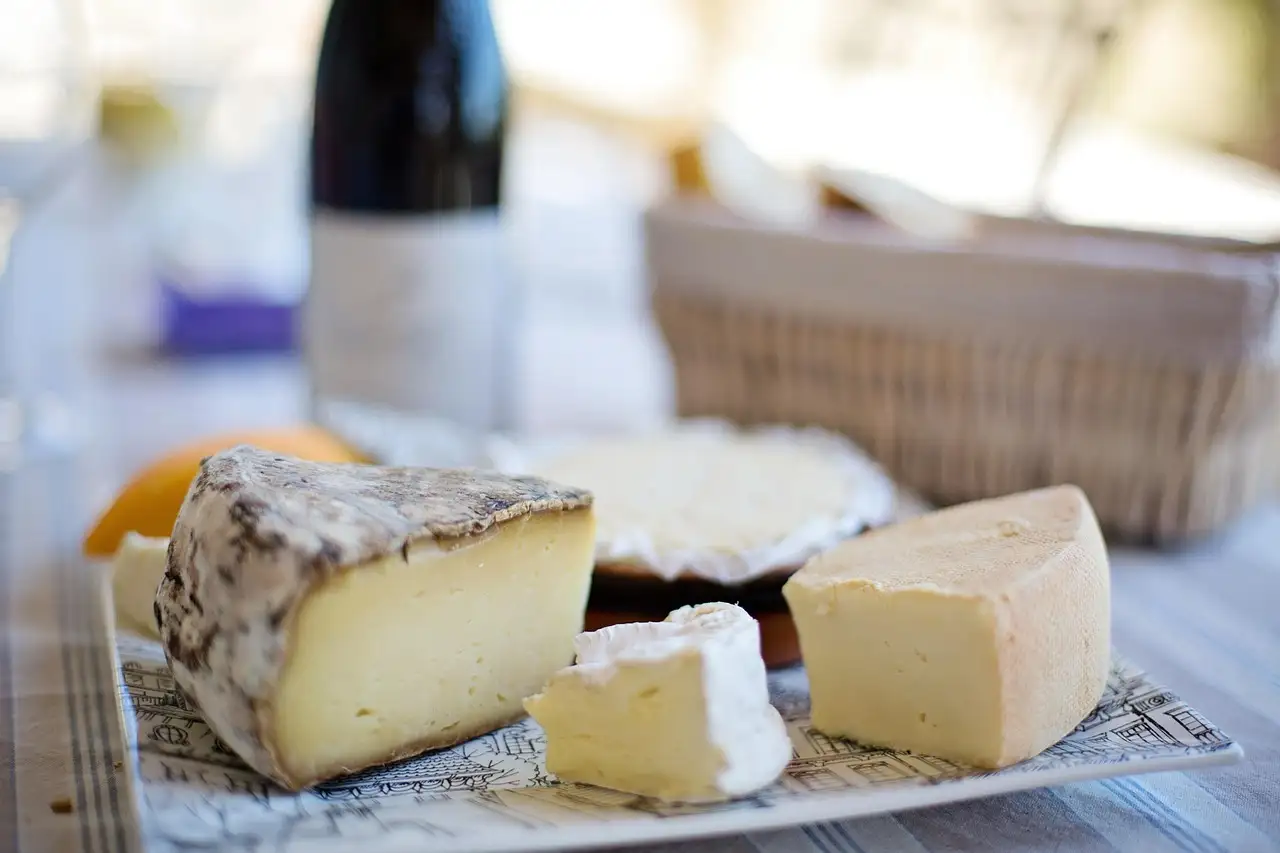 A board of French cheeses on a table with a bottle of wine behind