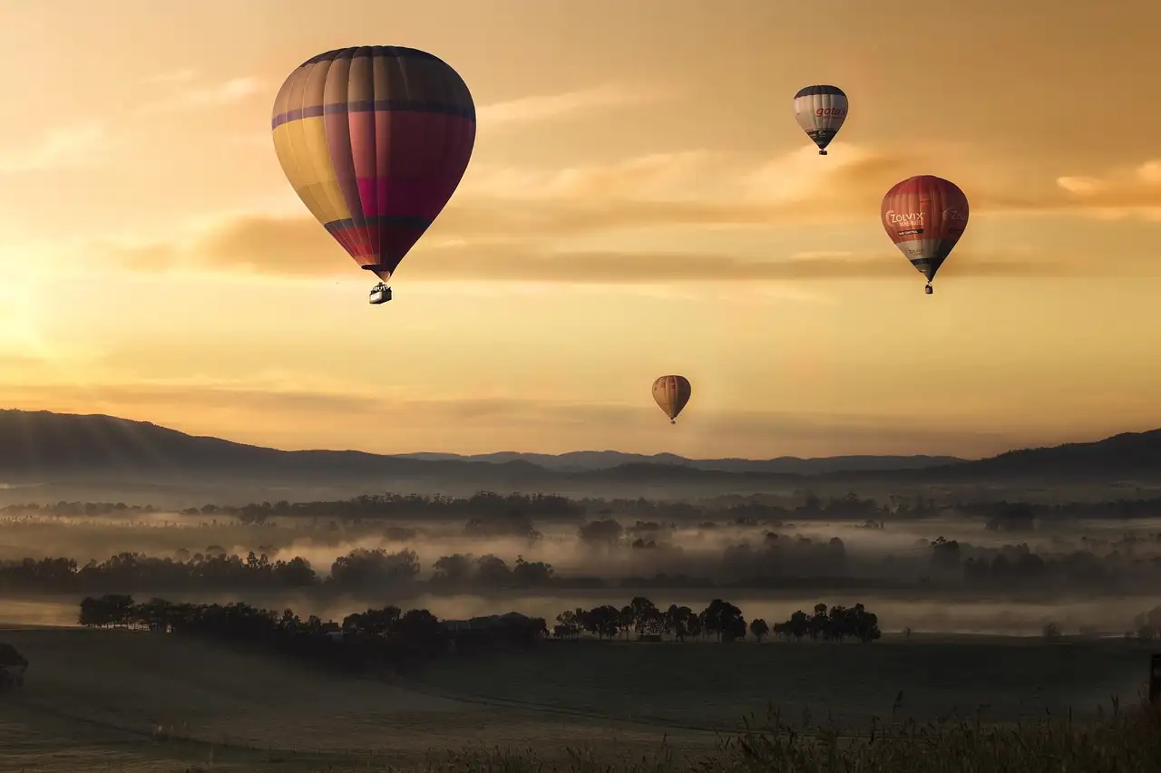 Hot air balloons floating over misty fields at sunset