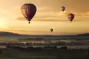 Hot air balloons floating over misty fields at sunset
