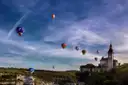 Hot air balloons above a church on a hillside in rural France