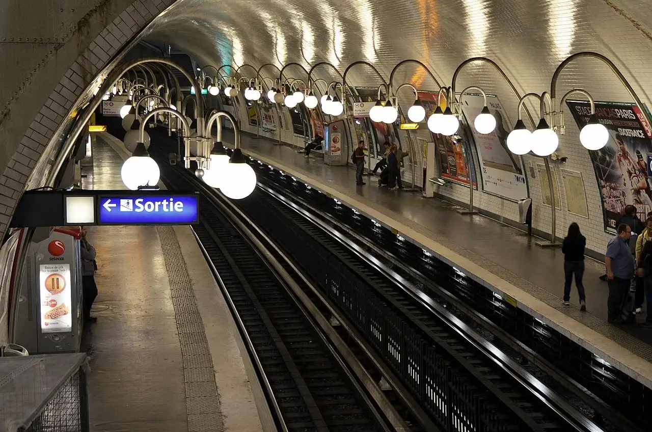 A curved, white-tiled Paris metro platform lined with globe lamps and an exit sign