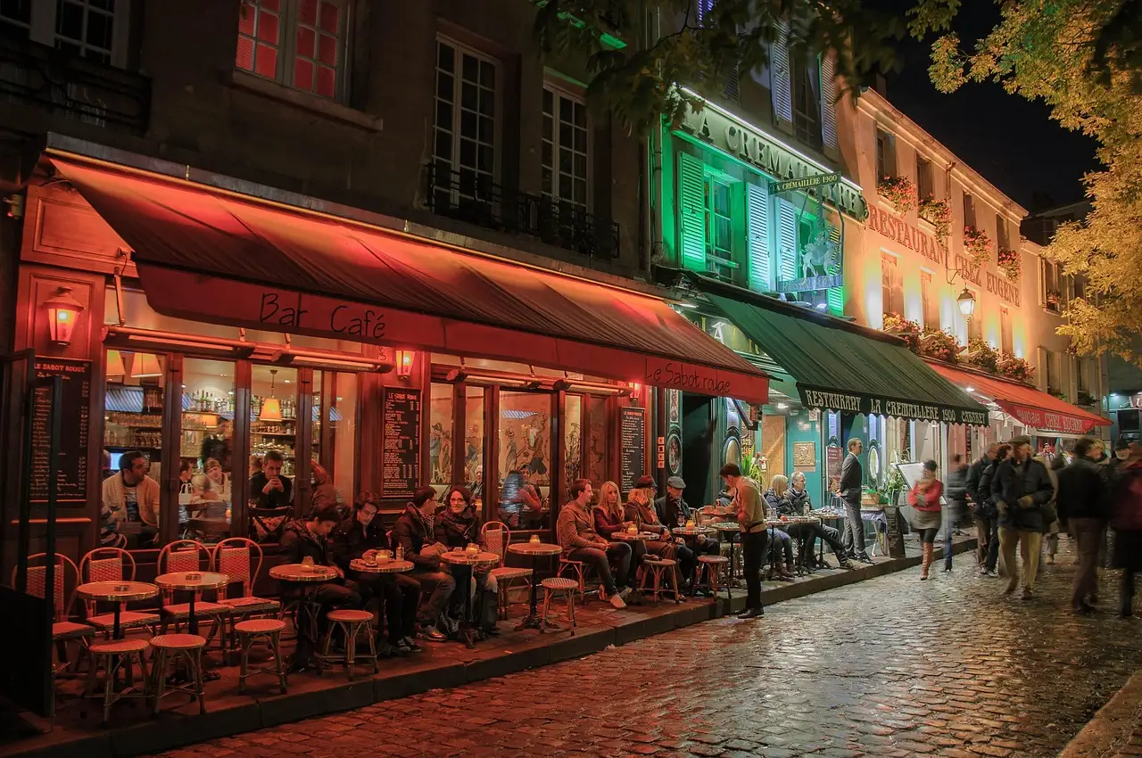 A lively Paris cafe terrace at dusk with red awnings along a cobbled street