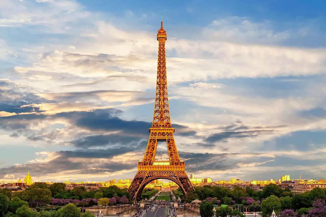 The Eiffel Tower lit by the evening sun under a cloudy sky with the Champ de Mars below