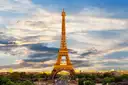 The Eiffel Tower lit by the evening sun under a cloudy sky with the Champ de Mars below