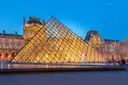 The Louvre glass pyramid glowing at blue hour in front of the palace