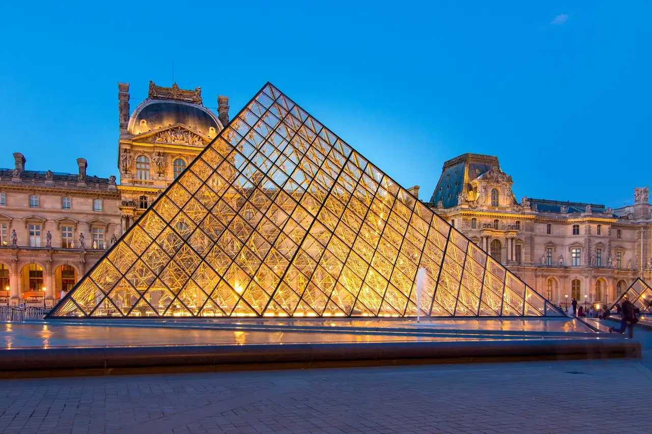 The Louvre glass pyramid glowing at blue hour in front of the palace