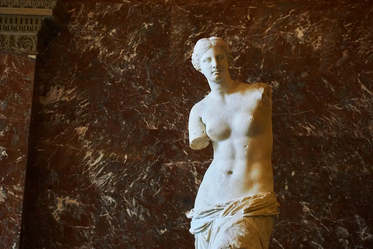 The Venus de Milo statue against a red marble wall in the Louvre