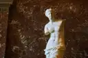 The Venus de Milo statue against a red marble wall in the Louvre