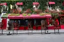 An ivy-covered red shopfront with café chairs in Rue des Rosiers, in the Marais