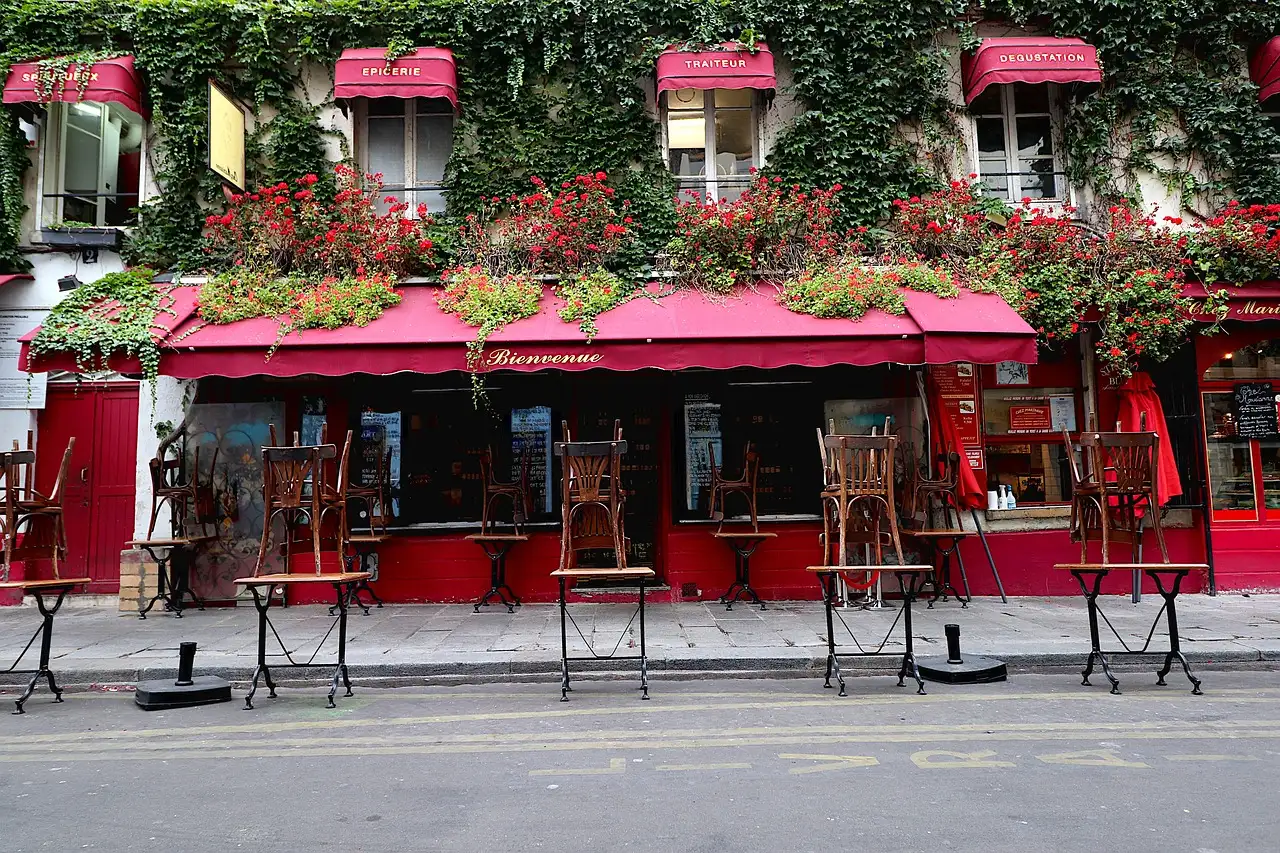 An ivy-covered red shopfront with café chairs in Rue des Rosiers, in the Marais