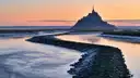 Mont-Saint-Michel silhouetted against a pink sunset over the bay