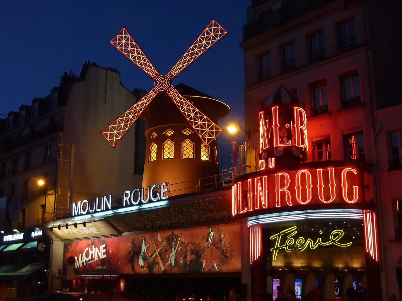 The Moulin Rouge lit up in red at night with its windmill turning above the street