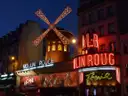 The Moulin Rouge lit up in red at night with its windmill turning above the street