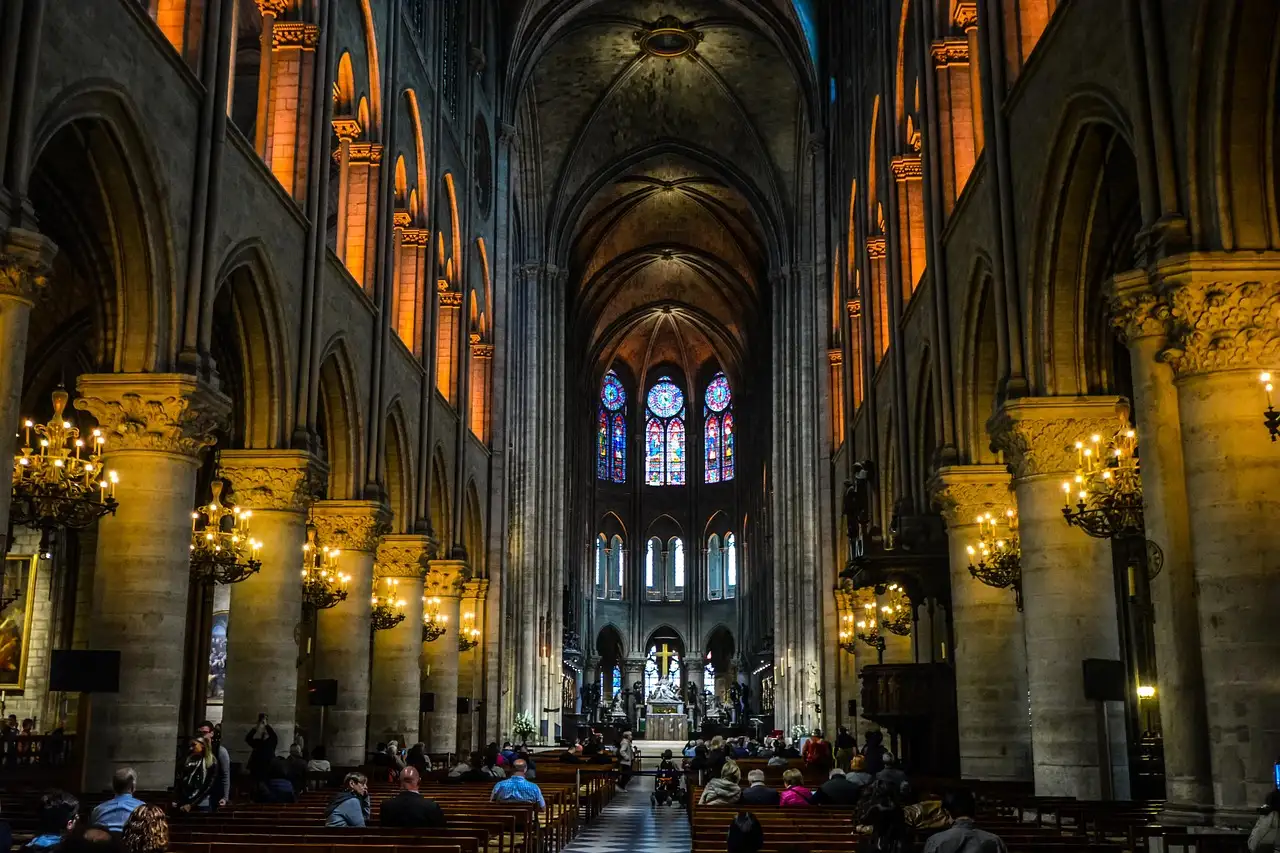 The long nave of Notre-Dame with stone pillars, chandeliers and visitors in the pews