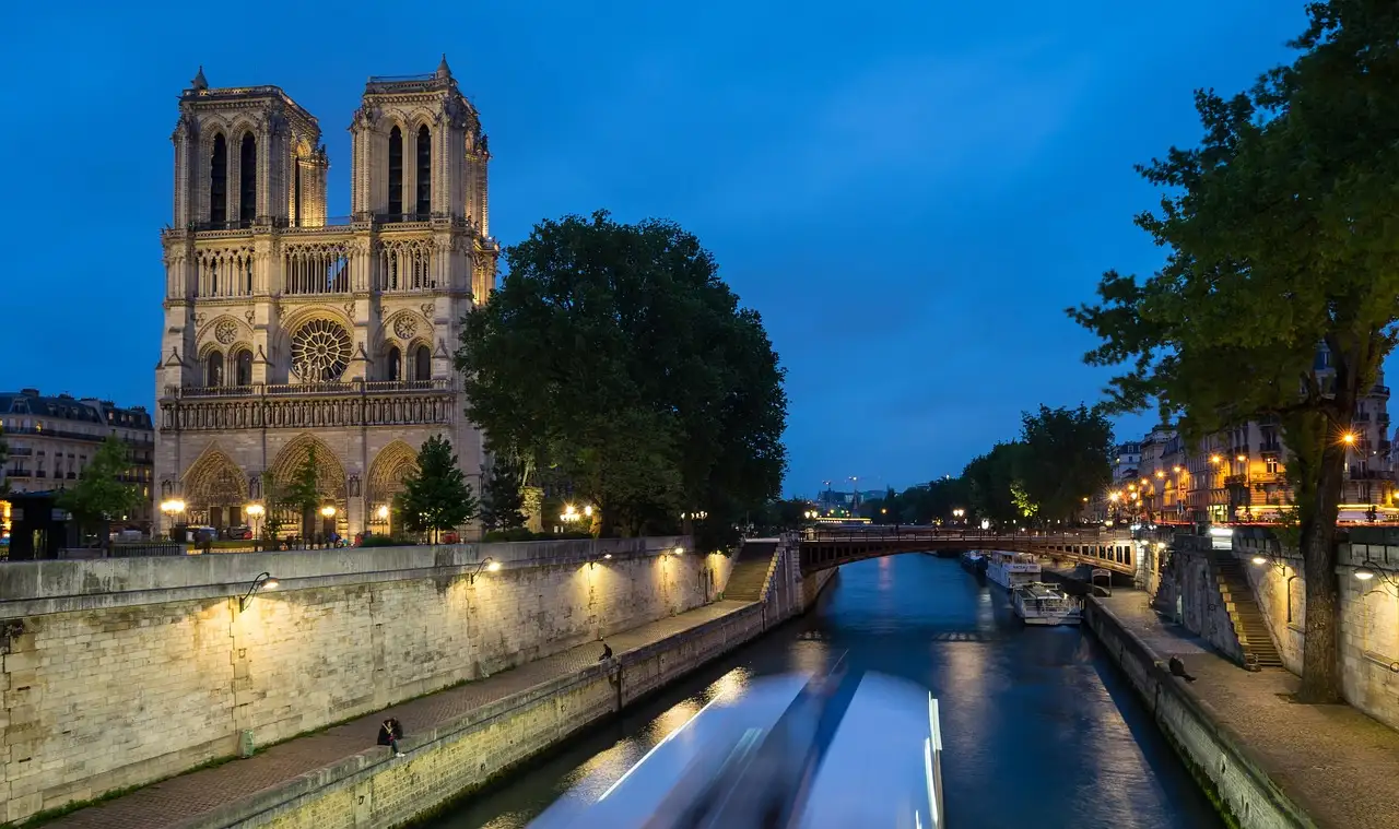 Notre-Dame lit at night above the Seine, with light trails of passing boats