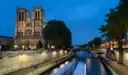 Notre-Dame lit at night above the Seine, with light trails of passing boats