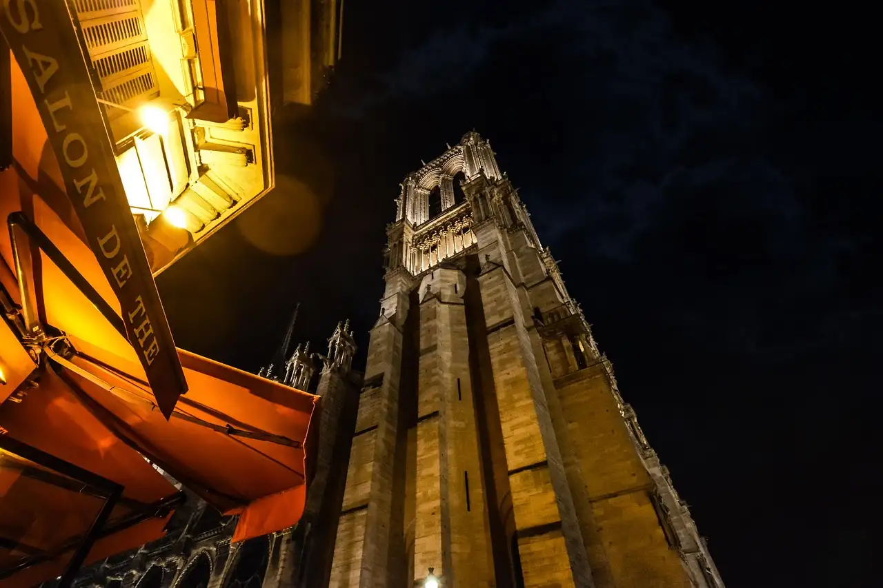 A Notre-Dame tower lit at night above a street café awning