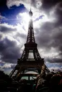 Passengers on the open top deck of a sightseeing bus below the Eiffel Tower