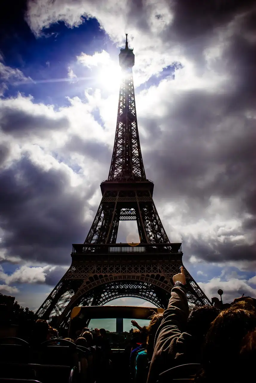 Passengers on the open top deck of a sightseeing bus below the Eiffel Tower