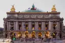 The front of the Palais Garnier at dusk with gilded statues and lit arcades