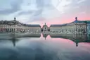 The Place de la Bourse in Bordeaux with its stone facades mirrored in the water at dusk