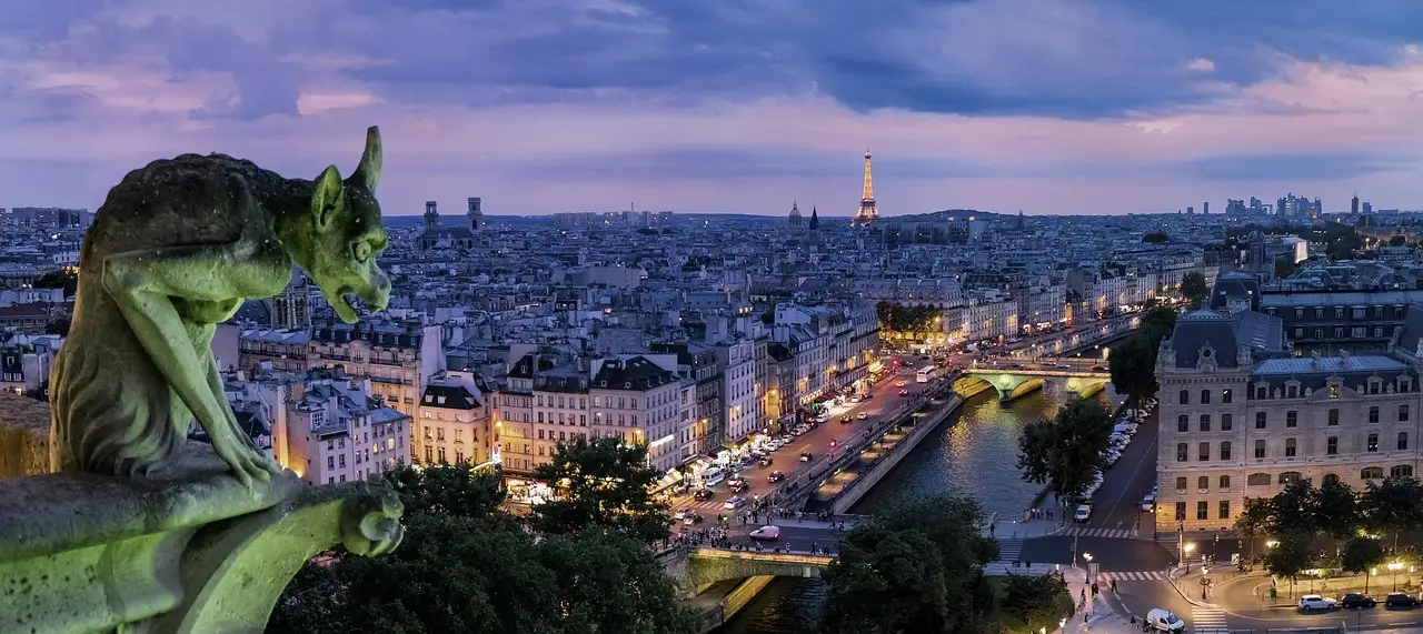 A Notre-Dame gargoyle looking out over Paris rooftops and the Seine toward the Eiffel Tower at dusk