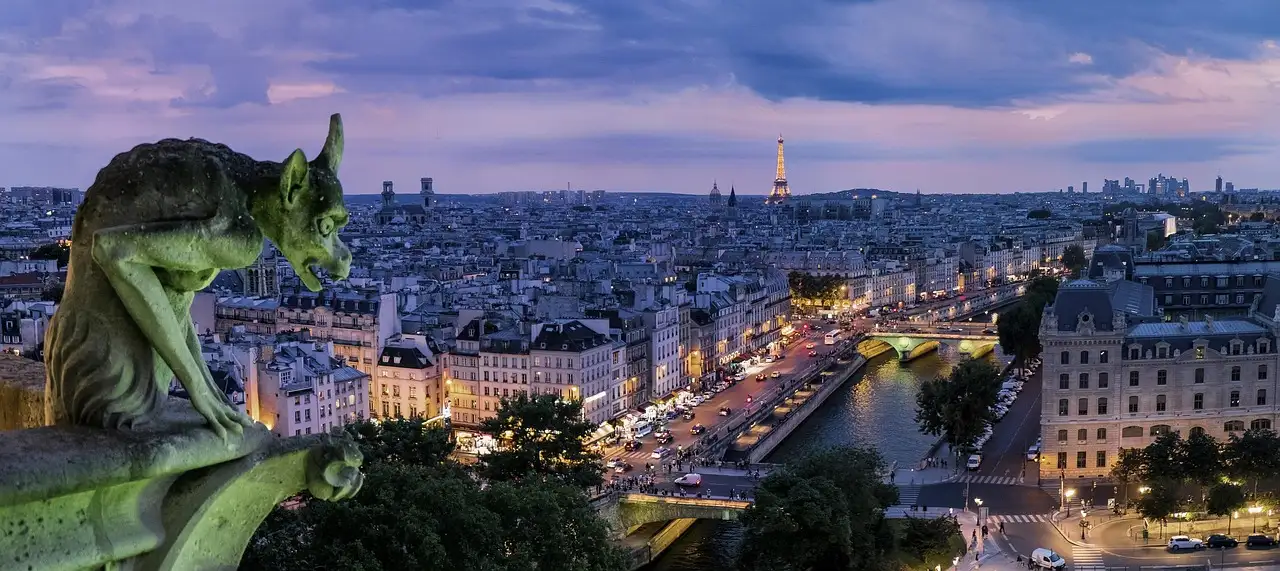 A Notre-Dame gargoyle looking out over Paris rooftops and the Seine toward the Eiffel Tower at dusk