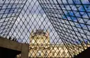 The Louvre's glass pyramid seen from below with the museum's stone wing behind it under a blue sky