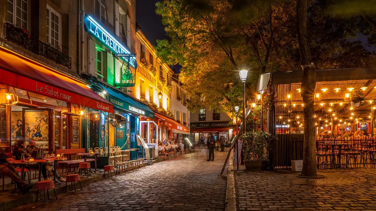 A cobbled Paris street lined with lit restaurant terraces at night
