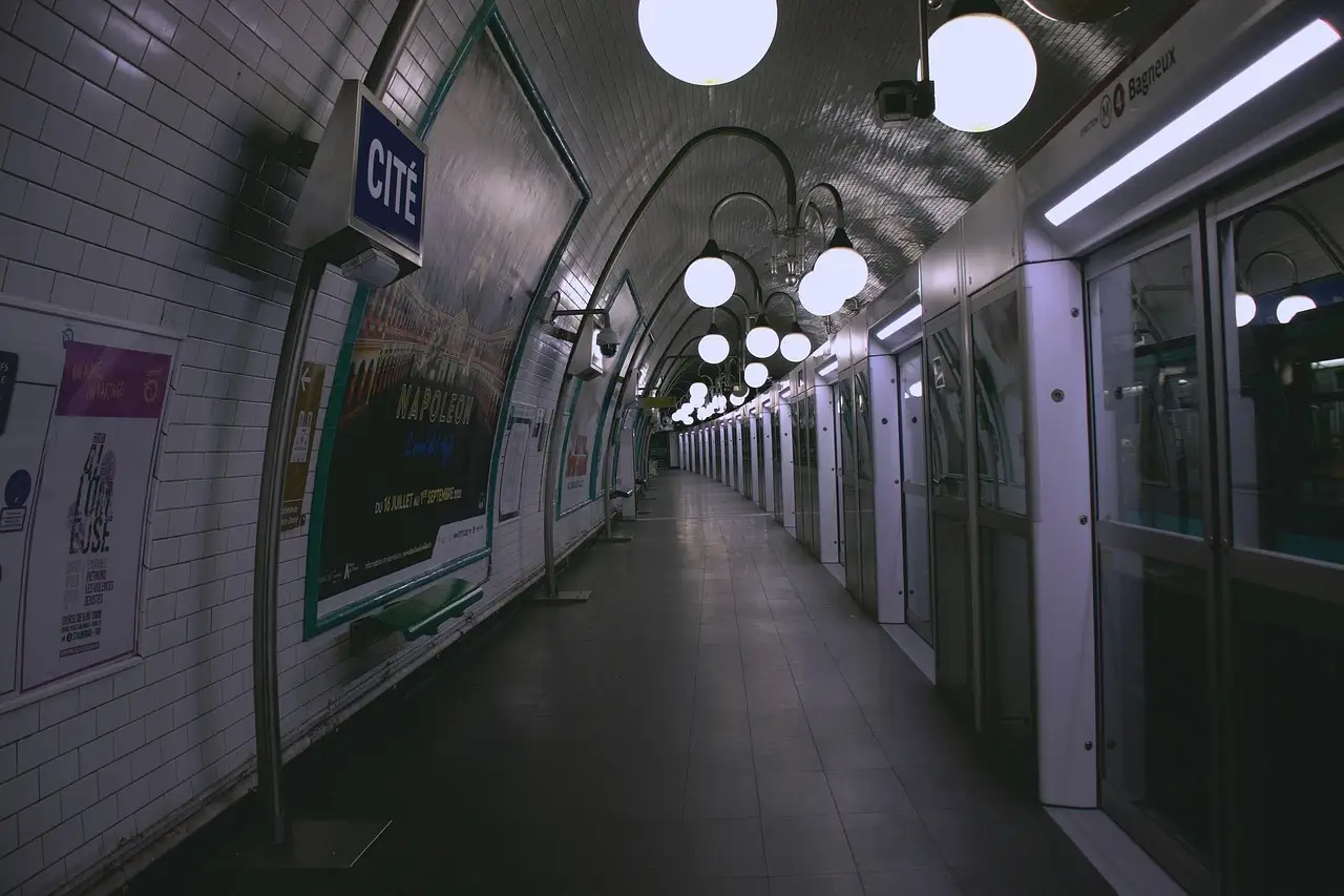 An empty, tiled Paris underground platform with globe lights and a train waiting at the doors
