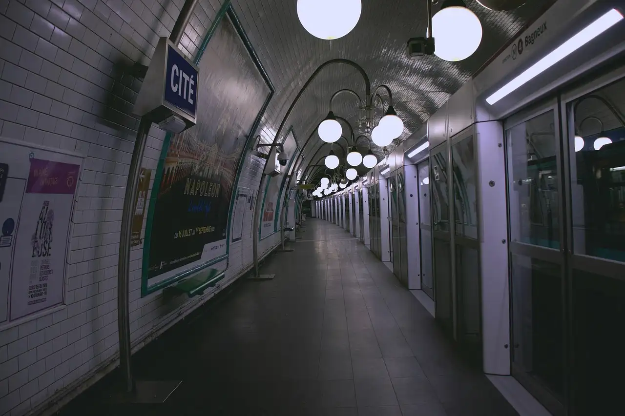 An empty, tiled Paris underground platform with globe lights and a train waiting at the doors